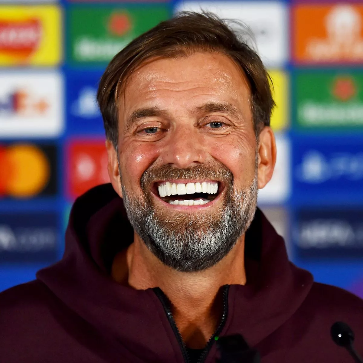 Jurgen Klopp smiling confidently during a press event, showcasing his bright and aligned teeth, part of his well-known charismatic public image.